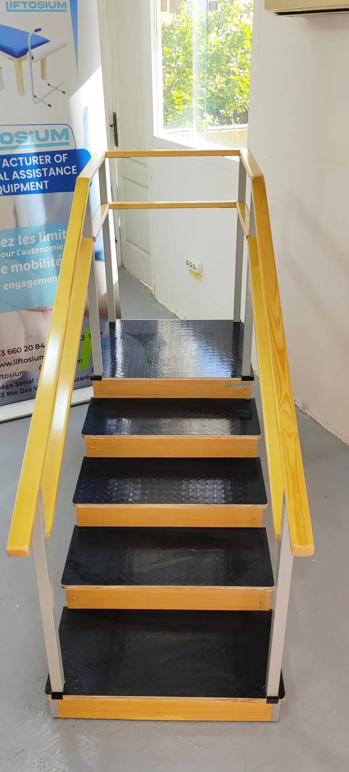 Vue de face de l'escalier de rééducation kinésithérapie Liftosium montrant les marches antidérapantes noires et les mains courantes parallèles en bois.